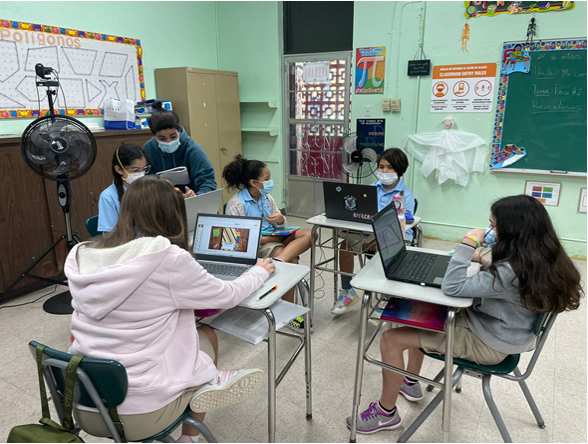 Grupo de seis estudiantes de escuela elemental sentadas en sus pupitres mientras trabajan individualmente en sus computadoras portátiles con la redacción de sus cuentos en el salón de clases.